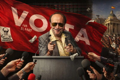 Santiago Segura as José Luis Torrente at a campaign podium surrounded by reporters in Torrente Presidente