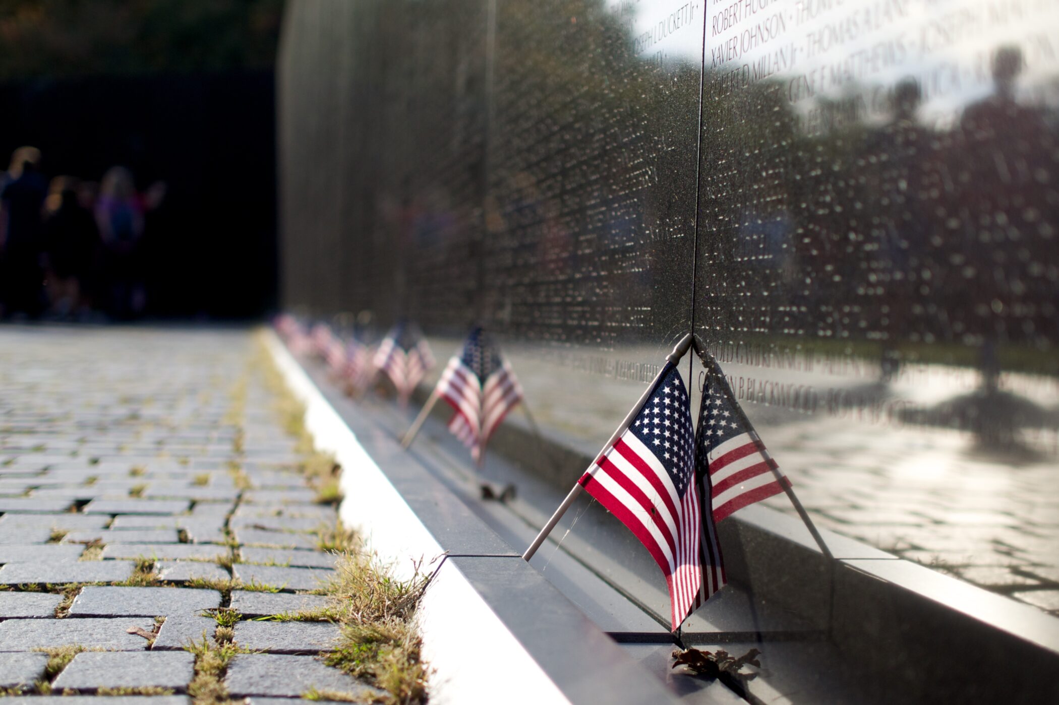 Small U.S. flags tucked along the base of the black granite Vietnam Veterans Memorial Wall, names engraved in the stone
