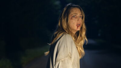 Jessica Rothe as Ellie, bloodied and disoriented on a dark road at night, in BT Meza's horror film Affection.