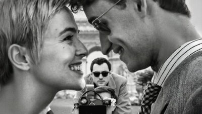 Zoey Deutch as Jean Seberg faces Guillaume Marbeck as Jean-Luc Godard in a black-and-white street scene from Richard Linklater's Nouvelle Vague.
