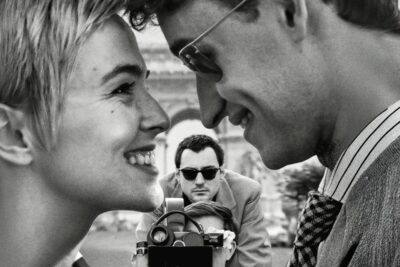 Zoey Deutch as Jean Seberg faces Guillaume Marbeck as Jean-Luc Godard in a black-and-white street scene from Richard Linklater's Nouvelle Vague.