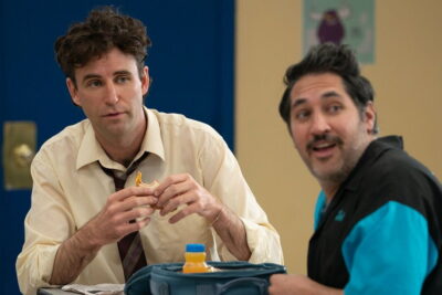 John Reynolds eats a packed school lunch beside a classmate in a high school cafeteria scene from the comedy Never Change!