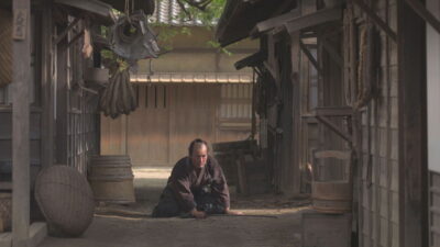 Kosaka Shinzaemon kneels on a recreated Edo-period street on a film set in Junichi Yasuda's A Samurai in Time.