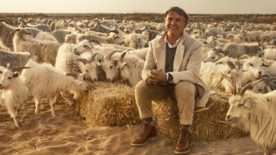 Brunello Cucinelli seated among cashmere goats in Giuseppe Tornatore’s documentary Brunello: The Gracious Visionary
