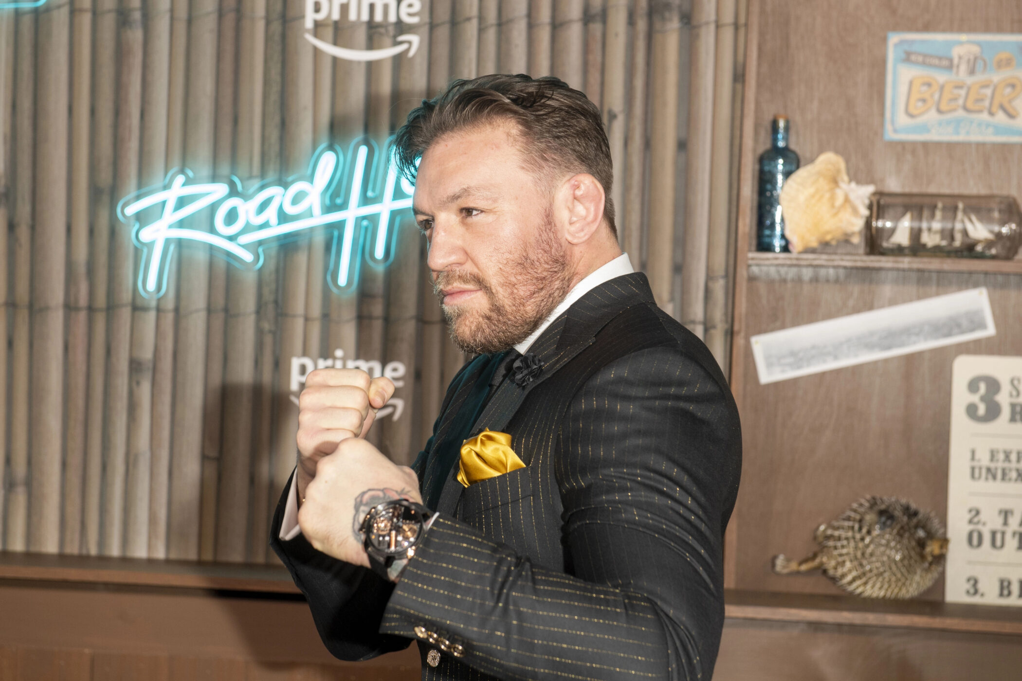Conor McGregor in a pinstripe suit raising his fists at the Road House premiere in New York