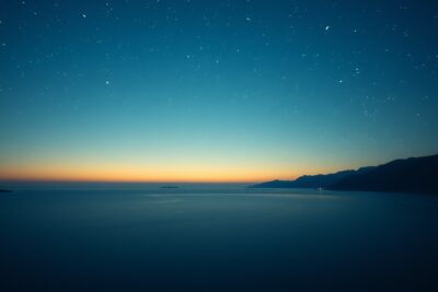 A single hand-cranked 70mm film strip unspooling into a starlit Aegean horizon, one frame