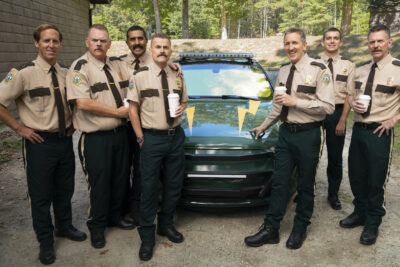 The Broken Lizard troupe in Jay Chandrasekhar's Super Troopers 3, in Vermont state-trooper uniforms beside their patrol cruiser.