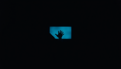 Silhouetted hand reaching toward a glowing blue screen in darkness — parasocial bonds in the digital age