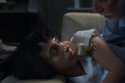 Nurse Eleni tends to an elderly patient holding a telephone handset in Georgia Bernstein's Night Nurse
