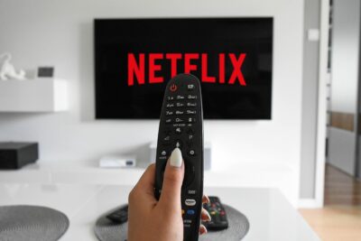 A hand points a TV remote at a screen showing a streaming service logo