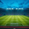 A floodlit, empty football pitch at dusk seen from high in the stand, the white line markings forming clean geometry across the green grass.