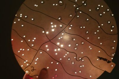 An aluminum plug plate from the Sloan Digital Sky Survey (SDSS), held up to light, showing hundreds of drilled holes that each position an optical fiber to collect light from a specific galaxy or celestial object.