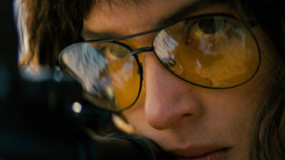 Adria Arjona as an Army sniper takes aim through amber-tinted glasses in Adam Wingard's Onslaught.