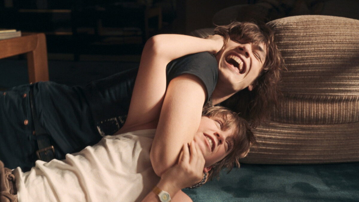 Two brothers play-fight on the floor in a scene from Just an Illusion, 2026