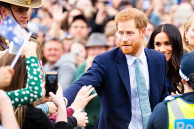 Prince Harry, Duke of Sussex, shaking hands with well-wishers in a crowd, with Meghan, Duchess of Sussex, beside him