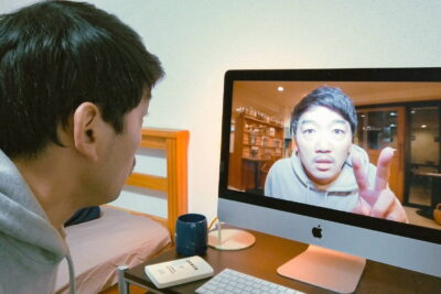 A still from Beyond the Infinite Two Minutes, Junta Yamaguchi's one-take time-loop comedy, showing a man watching his own image relayed two minutes into the future.