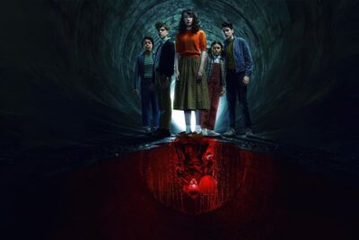 The young cast of IT: WELCOME TO DERRY standing in a sewer tunnel, with a reflection of Pennywise in red water below