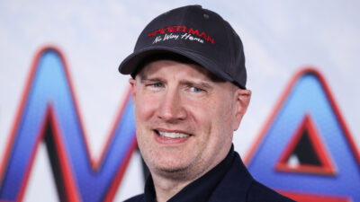 Kevin Feige smiling, wearing a Spider-Man: No Way Home cap, in front of the film logo backdrop