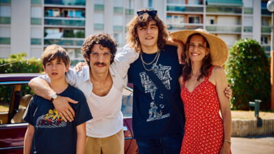 Louis Garrel, Camille Cottin and their two sons pose beside a car outside a suburban Paris apartment block in Olivier Nakache and Éric Toledano's Just an Illusion (2026).