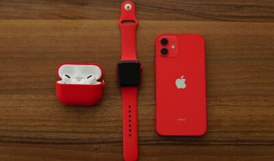 Apple AirPods Pro, Apple Watch, and iPhone in PRODUCT(RED) on wooden surface
