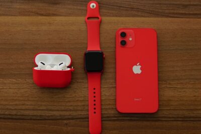 Apple AirPods Pro, Apple Watch, and iPhone in PRODUCT(RED) on wooden surface