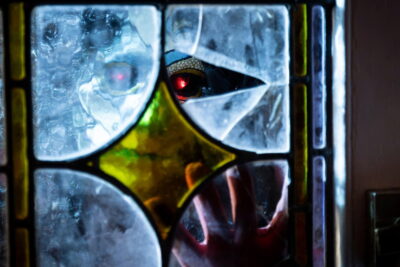 A clawed, red-eyed figure presses against stained glass in James Crow's horror film Harbinger