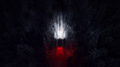 An overhead shot of a car threading a snow-covered forest road at night in Zach Cregger's Resident Evil.