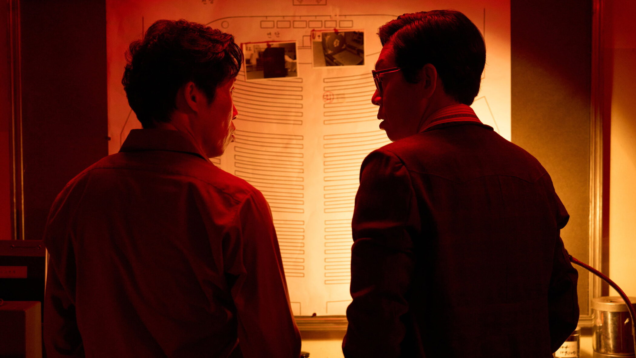 Two men study a seating plan in a red-lit darkroom in The Assassin(s), directed by Hur Jin-ho