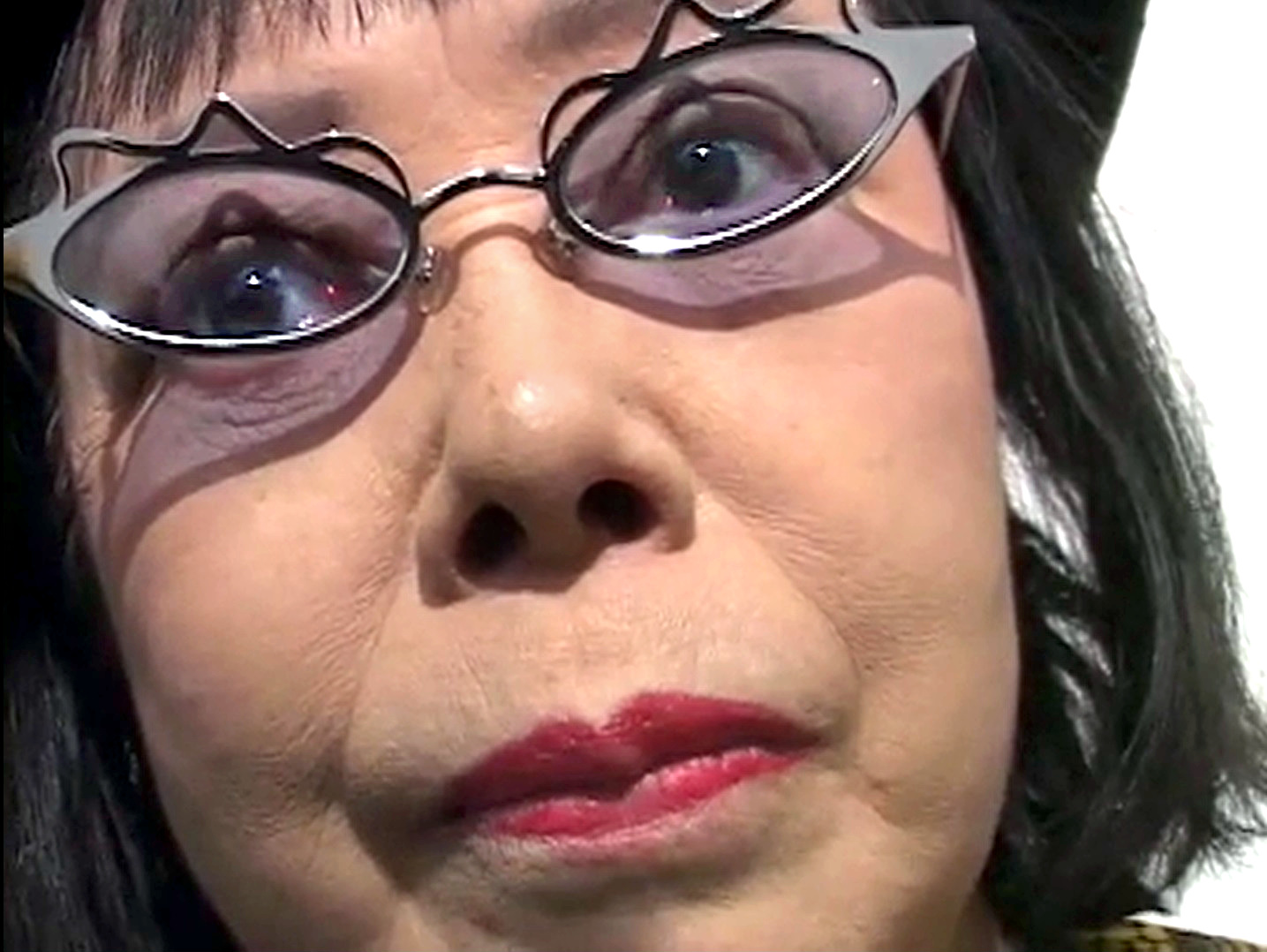 Close-up of Yayoi Kusama in tinted wire-framed glasses and red lipstick, video portrait by George Quasha, circa 2002-2005