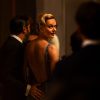 A woman in an open-back evening gown looks over her shoulder at a formal party in A Couple of Lies (Netflix)