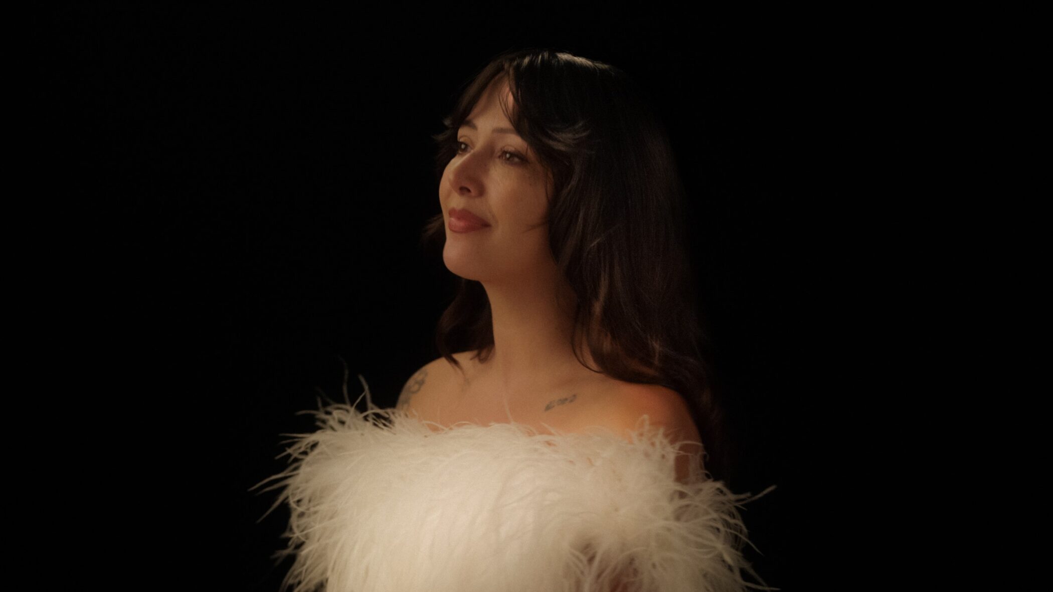 Folk singer Biita Houdei in a white feathered top against a black background