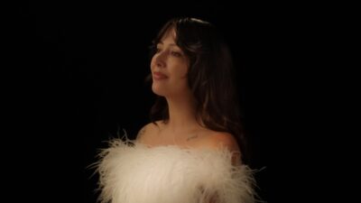 Folk singer Biita Houdei in a white feathered top against a black background