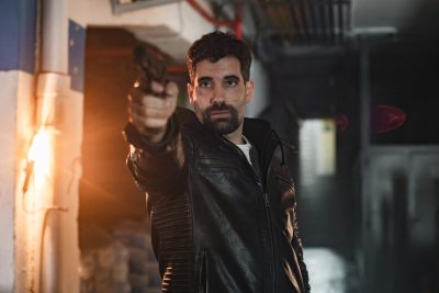 Un hombre con cazadora de cuero apunta con una pistola en un pasillo en penumbra en Collision Course