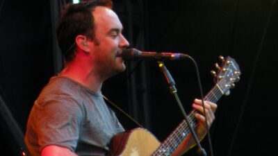 Dave Matthews singing into a microphone while playing acoustic guitar
