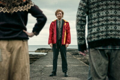 Domhnall Gleeson as Daniel faces two islanders on a stone jetty in Louis Paxton's The Incomer.