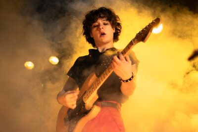 A young guitarist playing on a smoky stage in the Netflix film Less of a Stranger