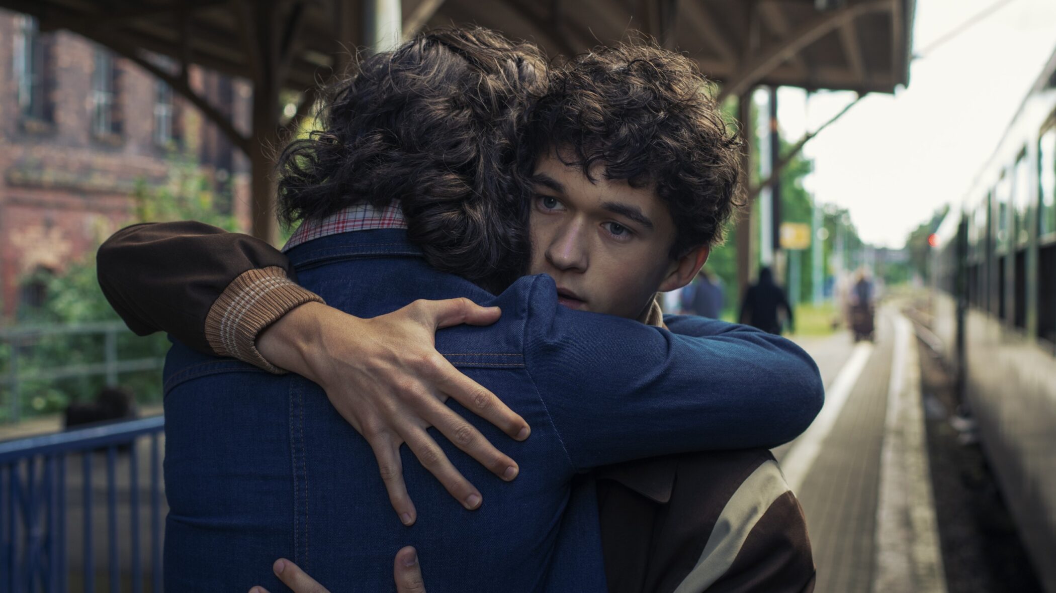 Two young men embracing on a train platform in the Netflix film Less of a Stranger