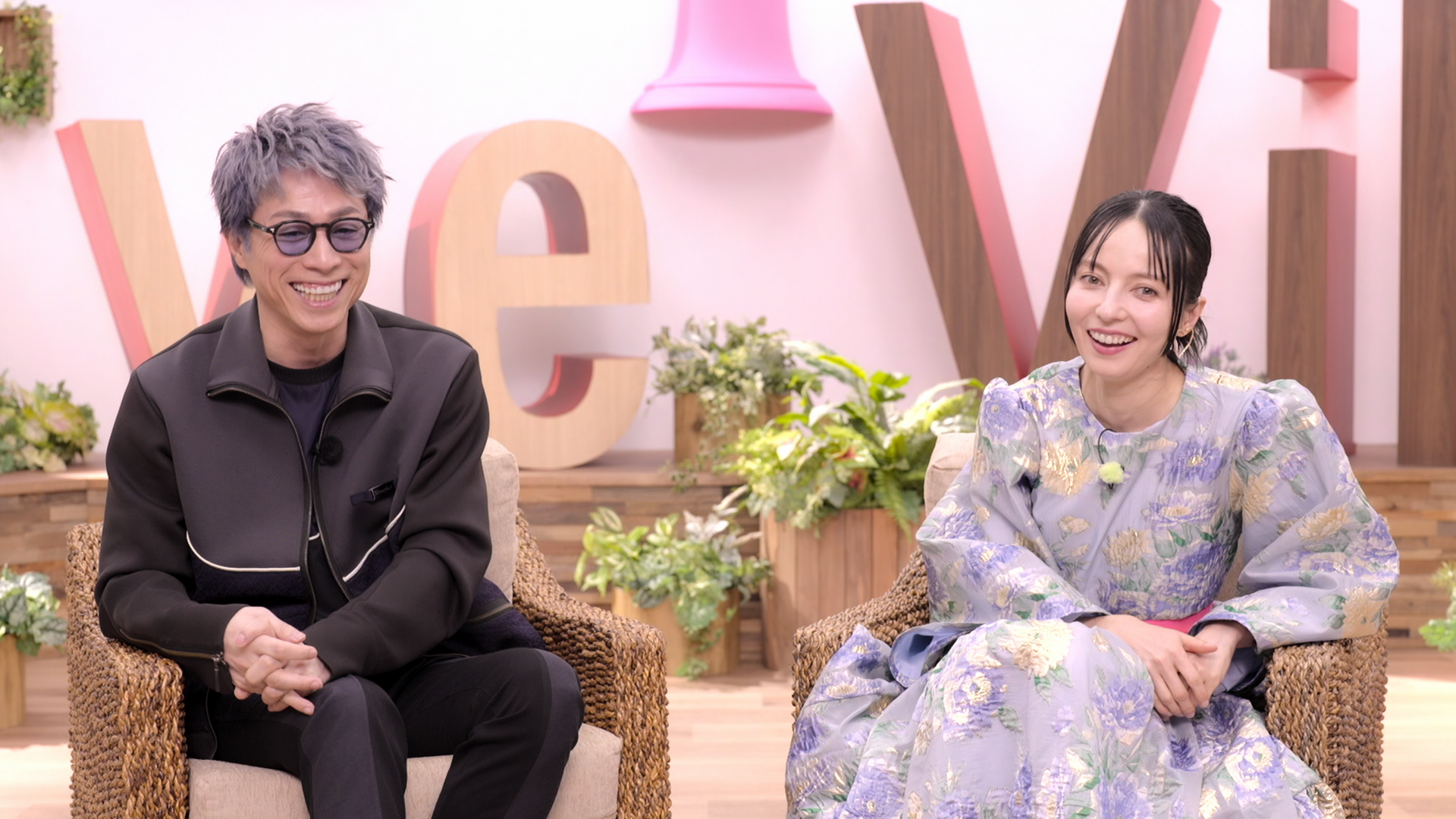 Studio hosts Atsushi Tamura and Becky seated in front of the Love Village letters