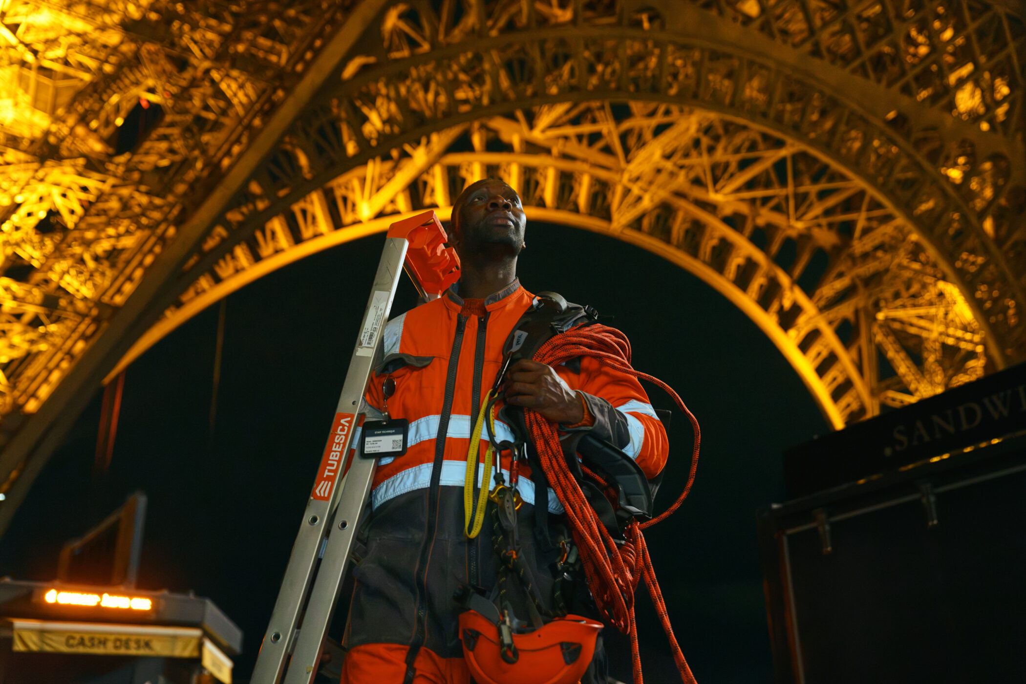 Omar Sy in a technician's high-vis jacket with ropes under the Eiffel Tower in Lupin