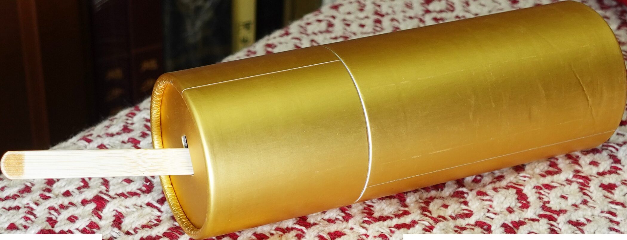 A gold divination cylinder with a bamboo stick poking out, lying on red and white cloth