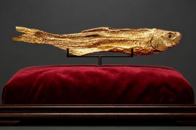 A salted fish covered in gold leaf displayed on a red velvet cushion