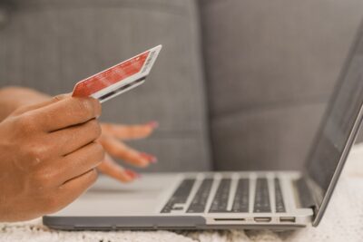 A shopper holds a credit card next to a laptop while paying for an online order — Kindel Media / Pexels