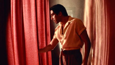 A young man parts a red curtain in a still from Marcelo Martinessi's Narciso