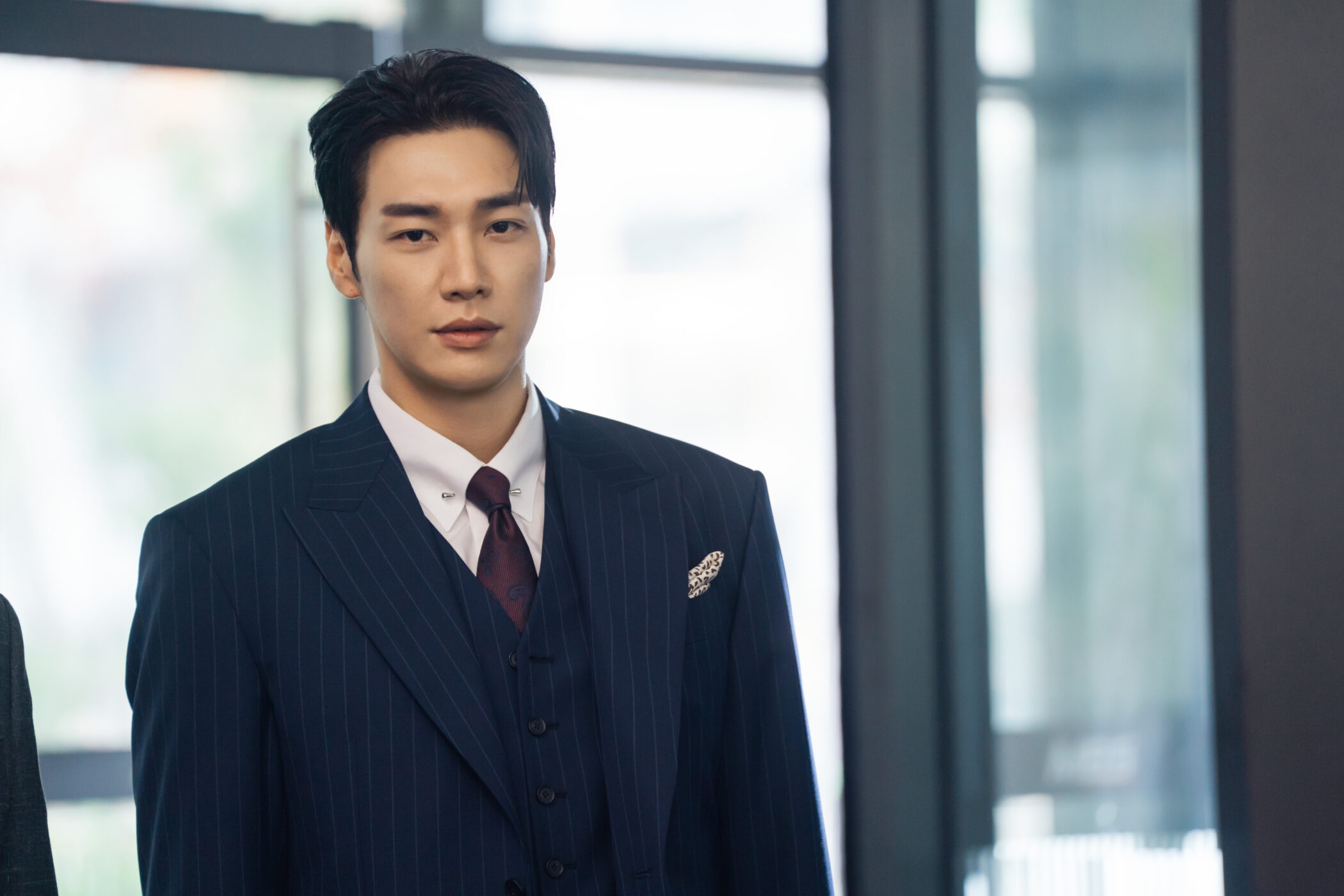 Un joven con traje de raya diplomatica de pie ante un ventanal en Take Charge of My Heart