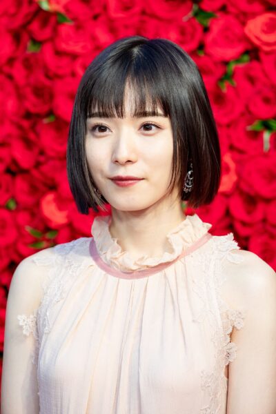 Mayu Matsuoka with a black bob and a pale pink ruffled sleeveless dress, posing in front of a wall of red roses at the opening ceremony of the Tokyo International Film Festival, 2018
