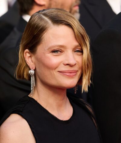 Mélanie Thierry smiling on the red carpet at the 2025 Cannes Film Festival, with a side-parted blonde bob, drop earrings and a black sleeveless dress