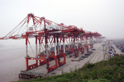 Red ship-to-shore container cranes lining a quay at Shanghai's Yangshan Deep-Water Port, with stacked shipping containers behind