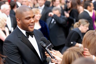 Tyler Perry in a tuxedo speaking to reporters on a red carpet