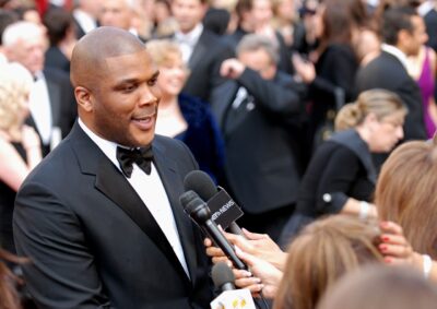 Tyler Perry in a tuxedo speaking to reporters on a red carpet