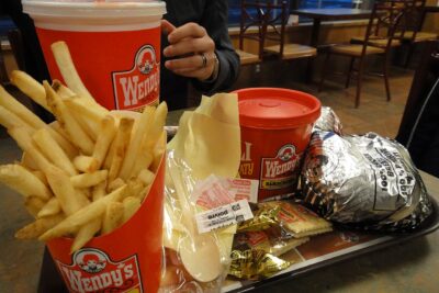 A Wendy's tray with fries, a large drink, a chili cup and a foil-wrapped burger inside a Wendy's restaurant